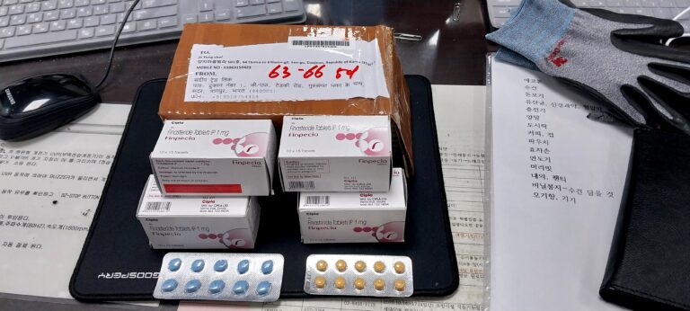Assorted pharmaceutical boxes labeled Finpecia Finasteride tablets on a desk with blister packs nearby and a computer keyboard in the background.