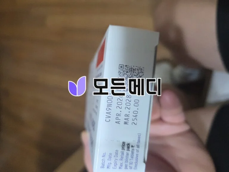 Close-up of a white product box with a QR code on the side, held by a hand; purple logo and Korean text overlay are visible.