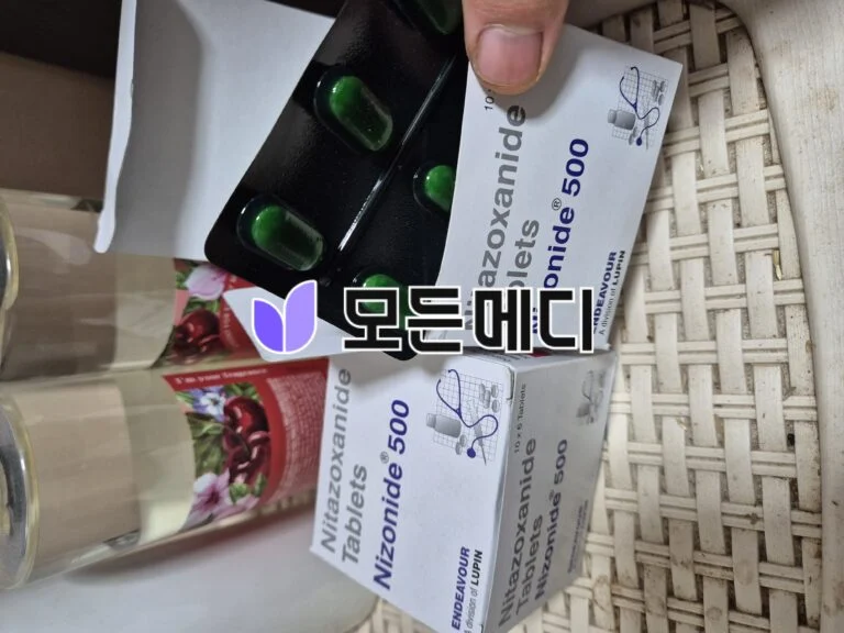 Blister pack containing green capsules placed on a white box of medication with '500' visible, on a woven basket surface.