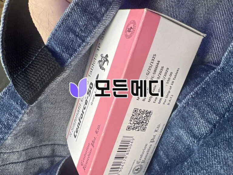 Pink-and-white medicine box resting on denim jeans, barcode and logo visible on the packaging.
