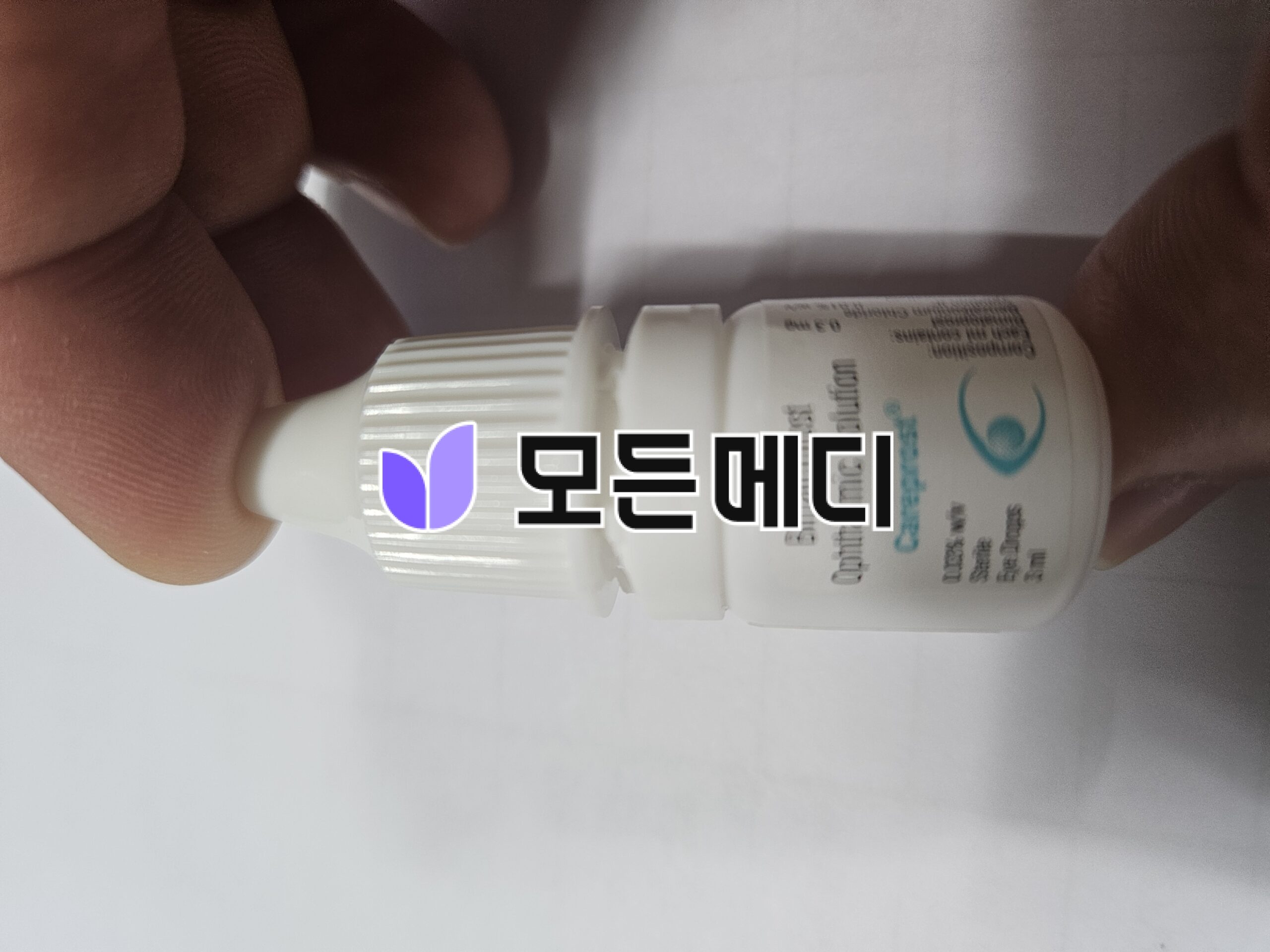 Hand holding a small white dropper bottle with a purple logo and printed text visible on the label.