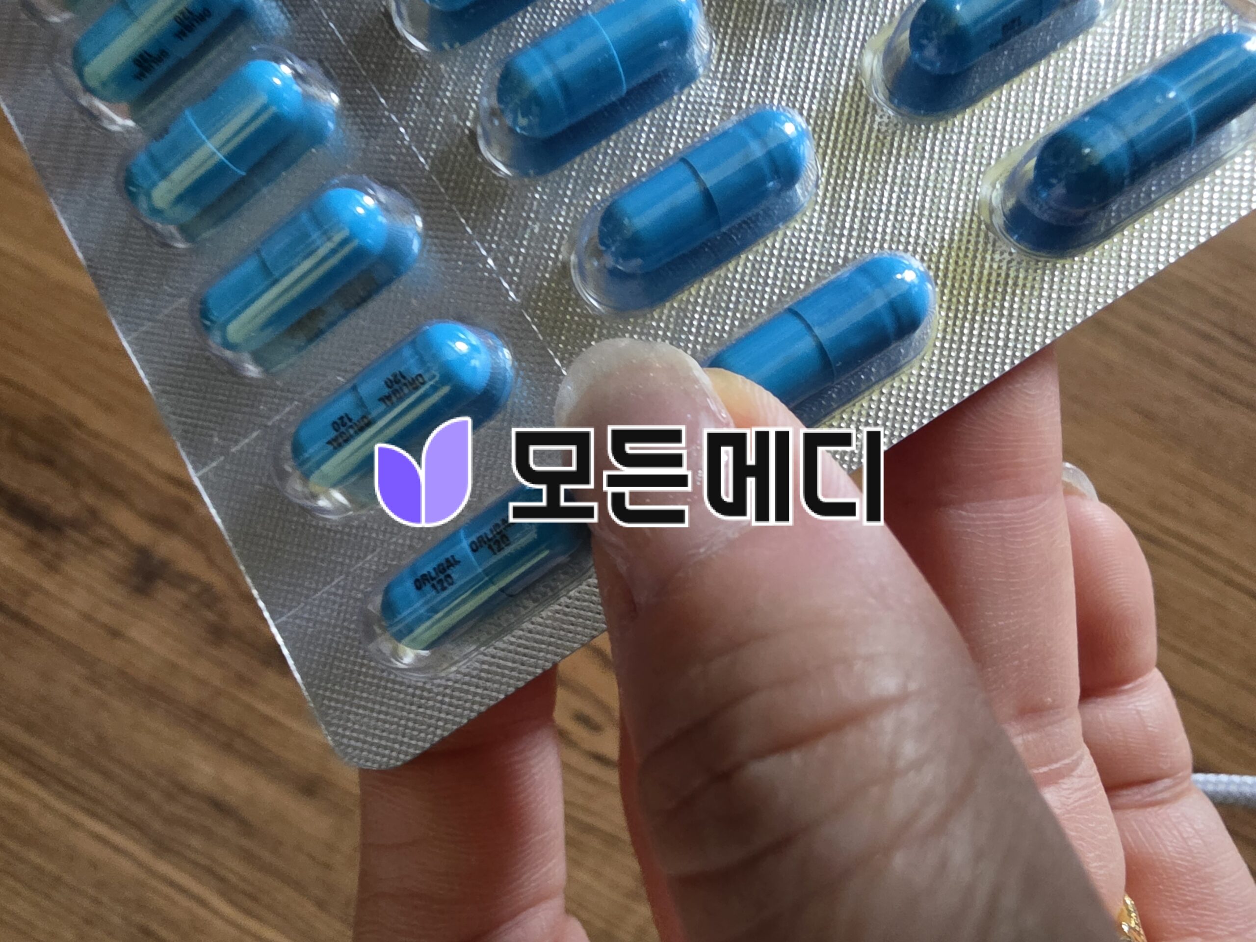 Blue capsules in a blister pack held between fingers, close-up view showing the medication form and packaging