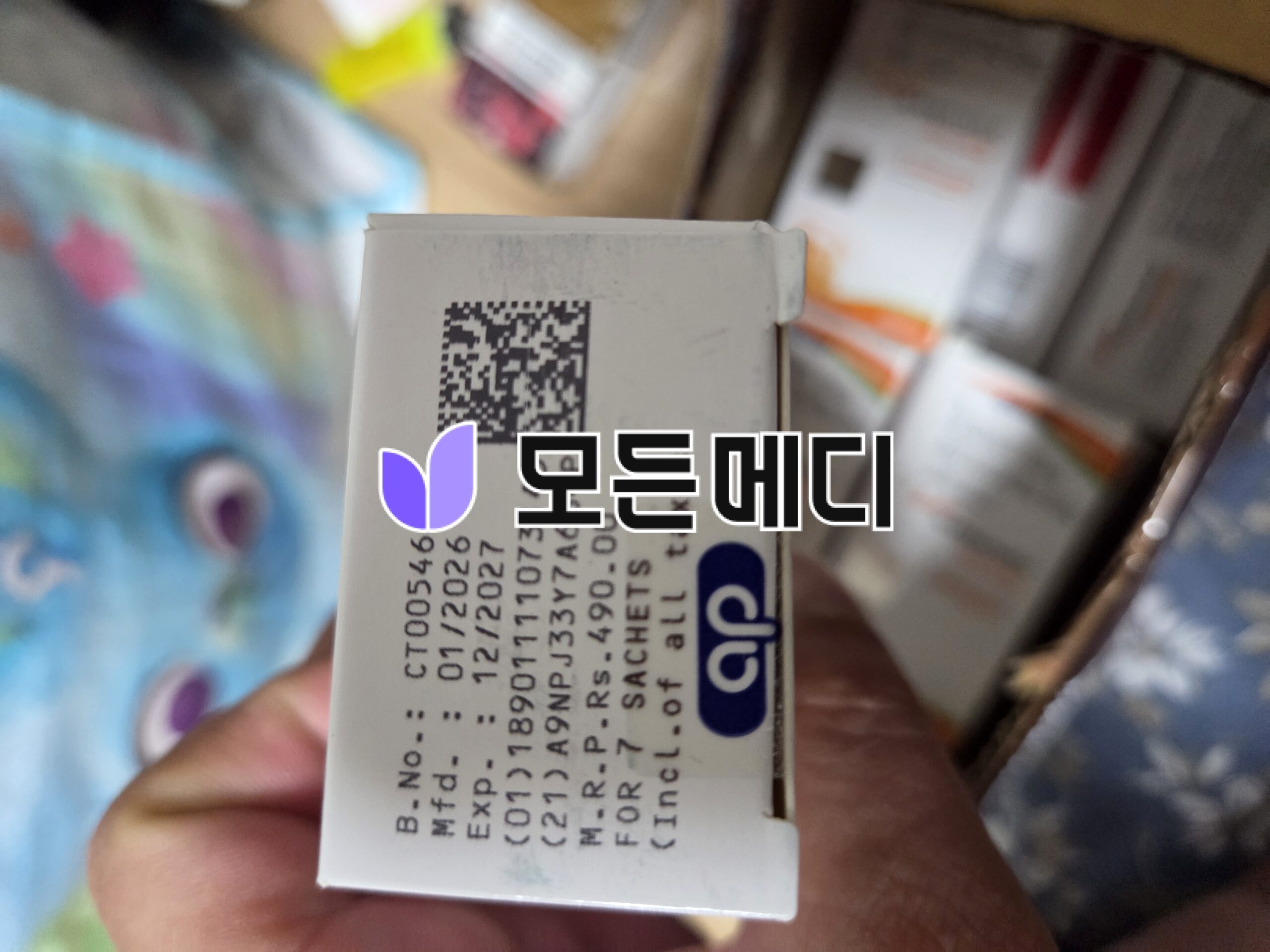 Close-up of a white box with a small QR code and a purple butterfly logo, held near a blurred store shelf.